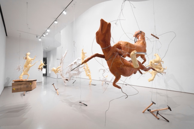 Large sculptures hanging from wire of yellow and white molds of foxes and coyotes with other industrial elements like hammers and wood