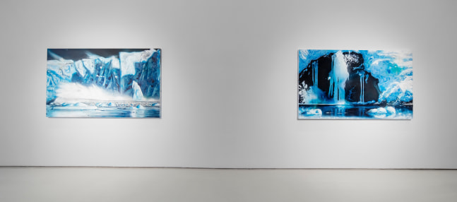 Two paintings of glaciers in shades of blue, white and black hang on a white wall
