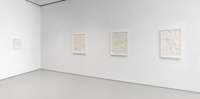Installation view of two adjacent walls featuring four white artworks on white walls