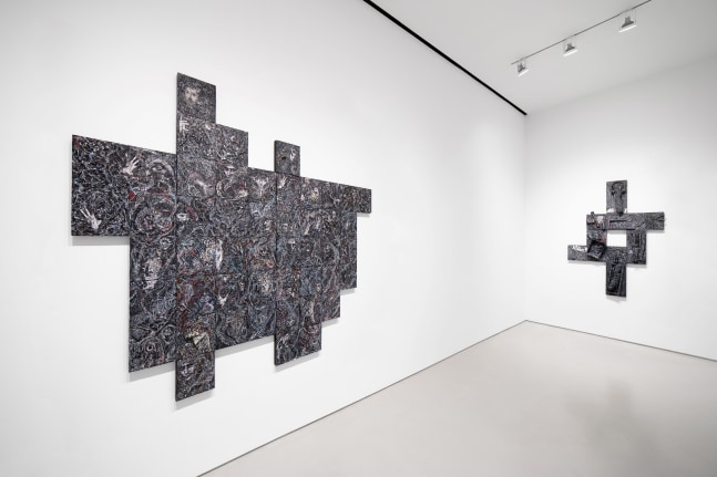 Dark, textured, geometric artworks hang on a white wall in a gallery space.
