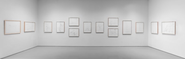 View of gallery with 14 framed drawings on white paper hanging on 3 white walls