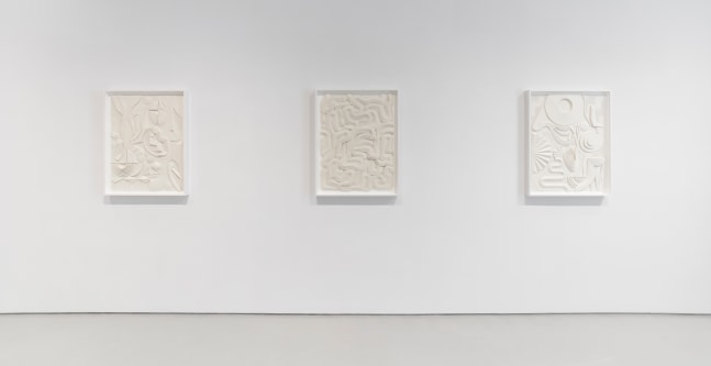 Installation view of three white artworks on a white wall