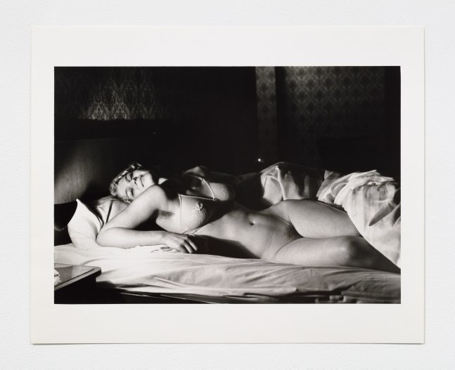 Black and white photographic print by Helmut Newton of a nude woman in bed