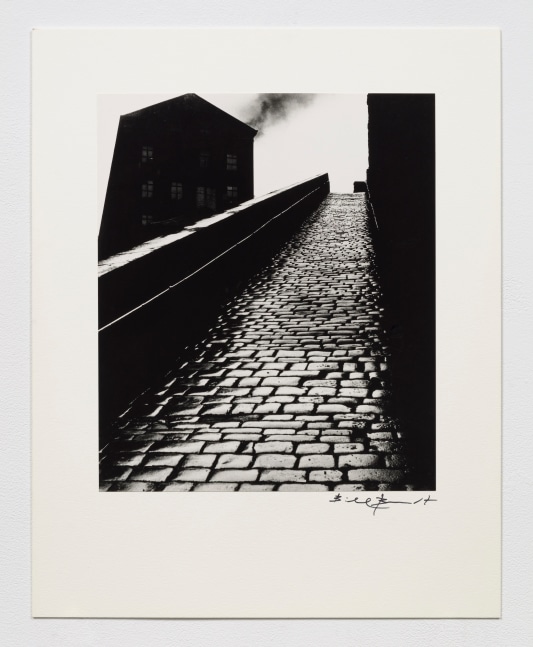 Black and white silver gelatin print of upward cobblestone hill with heavy contrasting shadows.