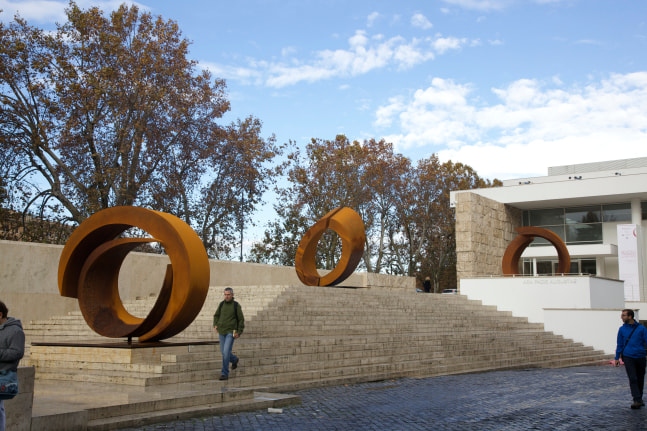 Two burnt orange circular sculptures by Beverly Pepper installed outside of a museum