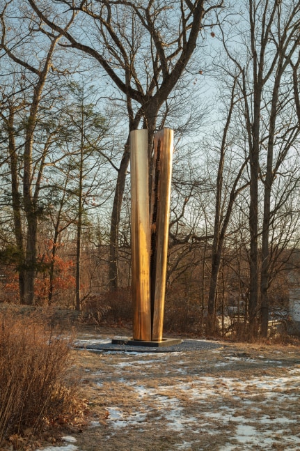 Outdoor installation view featuring a bronze sculpture by Arnaldo Pomodoro of a split column