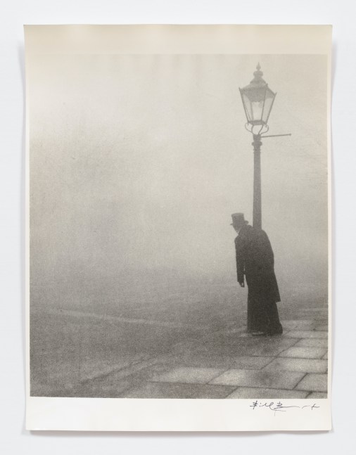Black and white silver gelatin print of man leaning on lamp post in fog.