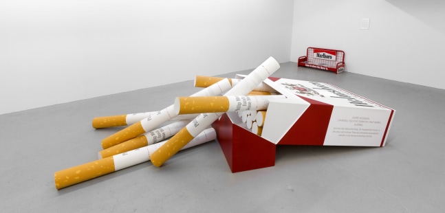 Hans Haacke Helmsboro Country, 1990 silkscreen prints and photographs on wood, cardboard and paper box: 30 1/2 x 80 x 47 1/2 in (77.5 x 203.2 x 120.7 cm); 20 cigarettes, each: 6 1/2 x 6 1/2 x 69 1/2 in (16.5 x 16.5 x 176.5 cm)