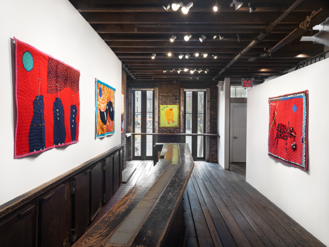 An image of four vibrant quilts in the gallery lobby with the window in view