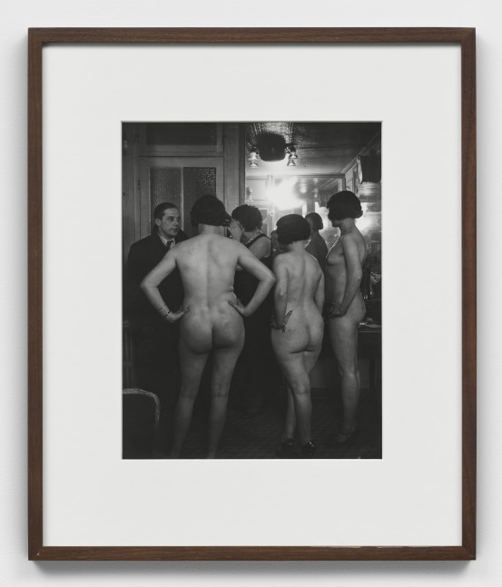 A black and white photographic print by Brassai depicting the introduction of multiple nude women and a clothed man at Suzy's