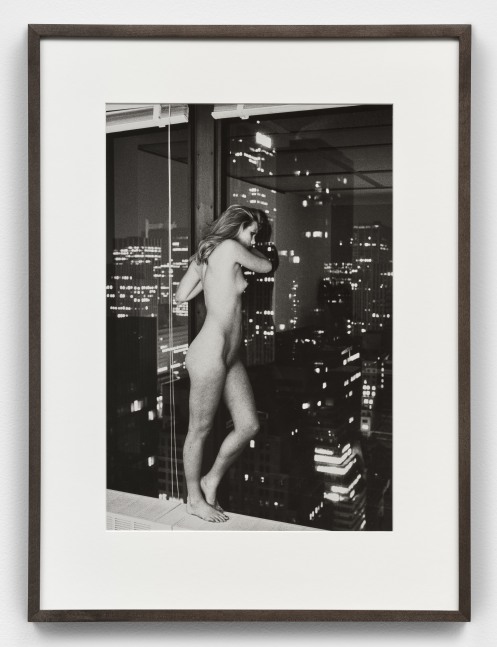Black and white photographic print of Patti Hansen standing nude and overlooking Manhattan from a window