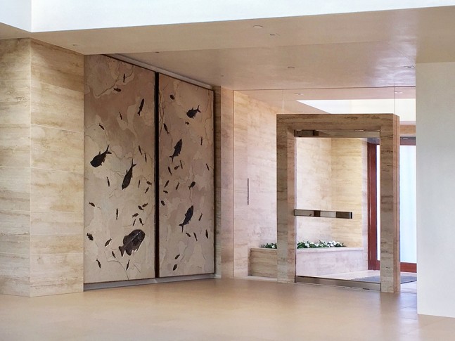 A giant fossil duptich mural containing large and small fossil fish sits just inside the entryway of a modern home