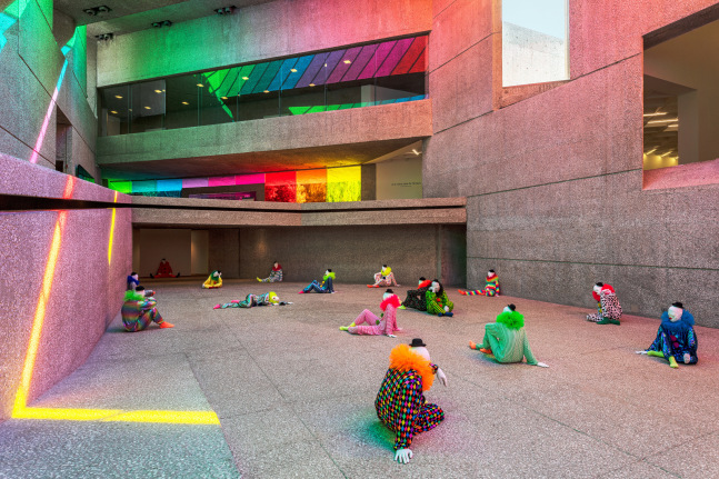 Installation view of colorful clown sculptures and rainbow colored windows by Ugo Rondinone