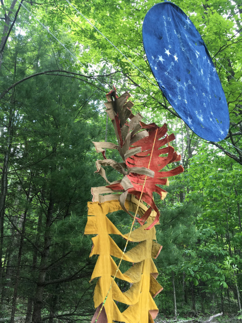 Color photograph of an outdoor textile sculptural installation by Joy Curtis, colored with natural dyes and installed high up hanging from the trees, installed at the Al Held Foundation, 2021. Exhibition curated by Alyson Baker and River Valley Arts Collective