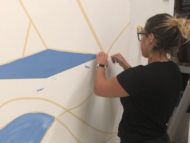 Student experimenting with Al Held's process of drawing geometric shapes with masking tape on a large canvas.