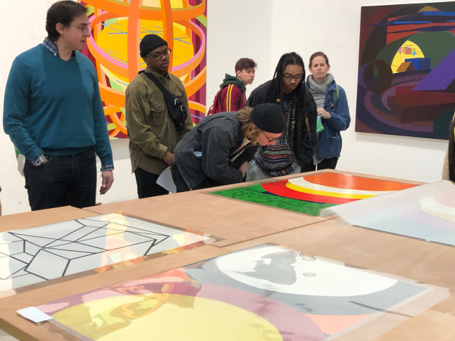 A group of students discuss colorful abstract prints and paintings by Al Held.