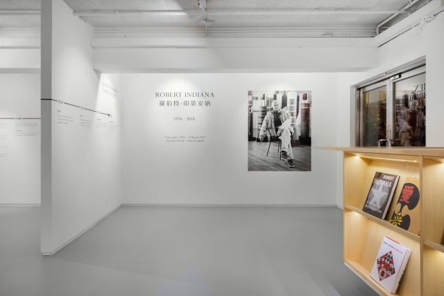 View of entry area to the exhibition Robert Indiana at Ben Brown Fine Arts, Hong Kong, December 7, 2021–March 8, 2022. A large photo of Indiana accompanies the exhibition wall text, and books about Indiana are visible.