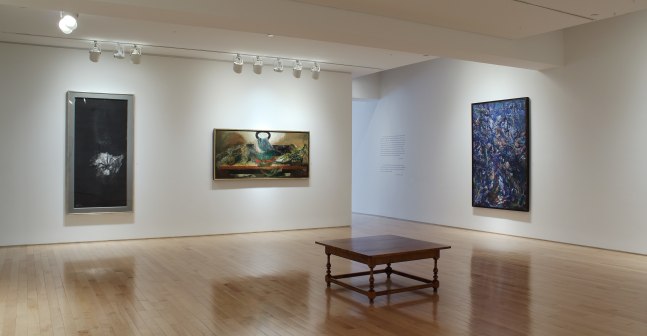 Photograph showing a corner view of an exhibition space with three paintings hanging on white walls