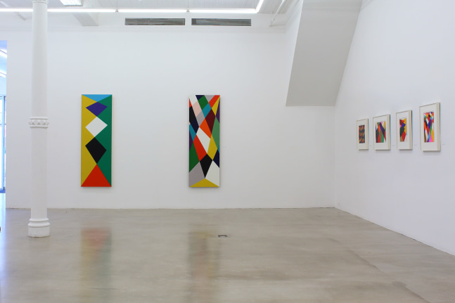 Photograph showing a corner view of an exhibition space, with six paintings hanging on white walls