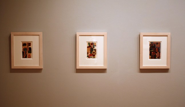Photograph showing a view of an exhibition, with three small framed paintings hanging on a grey wall