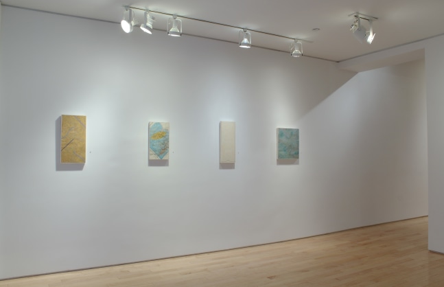 Photograph showing a corner view of an exhibition space, with four paintings hanging on white walls