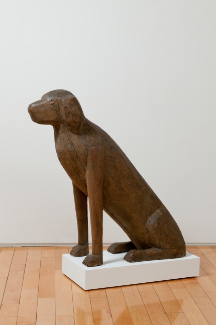 Side view of a wood sculpture of a tall dog sitting on its hind legs