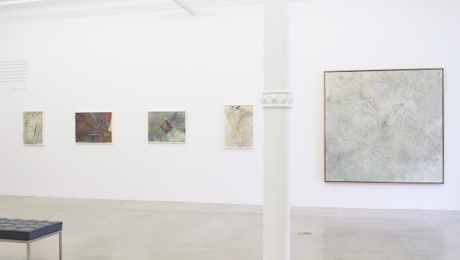 Photograph showing a view of an exhibition space, with five paintings hanging on a white wall