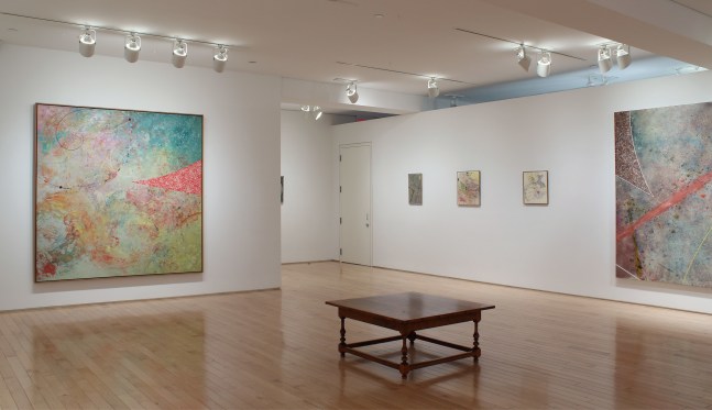 Photograph showing a corner view of an exhibition space, with five paintings hung on white walls