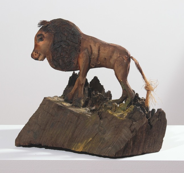 Wooden sculpture of an abstracted lion standing on a hill, with a piece of rope as its tail
