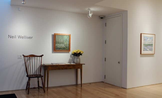 Photograph showing a view of an exhibition space, with one painting hanging on a white wall over a table a chair