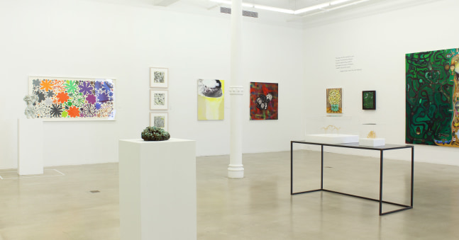 Photograph of a corner view of an exhibition showing a range of paintings, drawings, sculptures and prints in a white gallery space