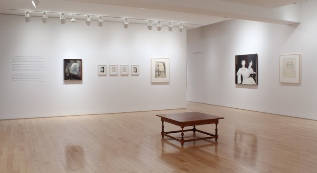 Photograph showing a corner view of an exhibition space, with eight paintings hanging on white walls