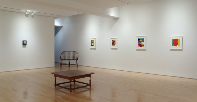 Photograph showing a corner view of an exhibition space, with five paintings hung on white walls