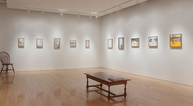 Photograph showing a corner view of an exhibition space, with eleven small paintings hanging on white walls