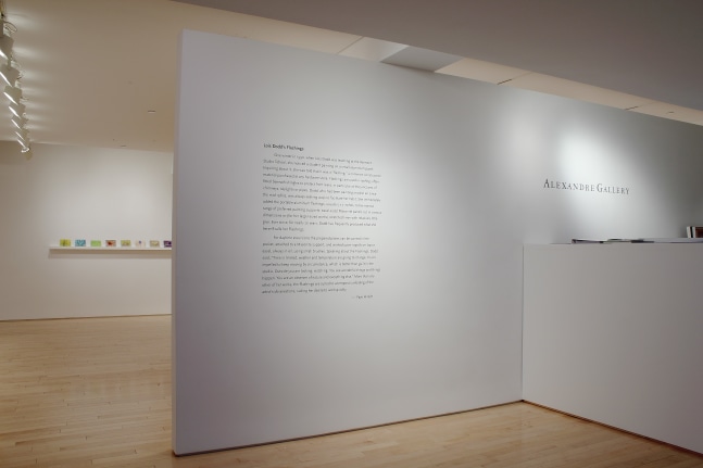 Photograph showing a front view of an exhibition space, with text describing the exhibition on a white wall