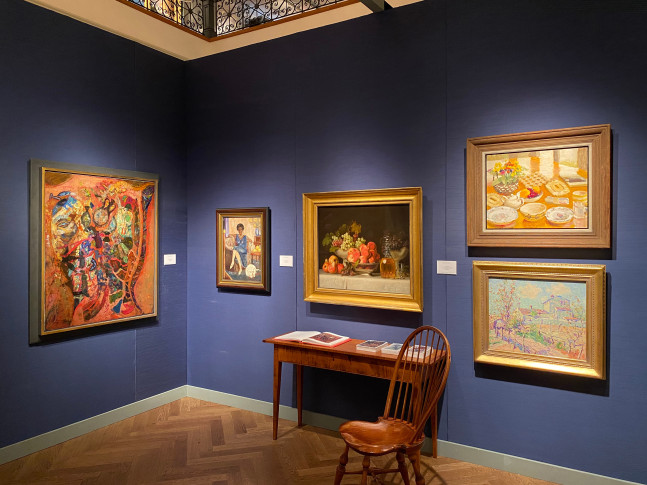 Photograph of a corner view of an exhibition showing five paintings in various styles hanging on a blue wall