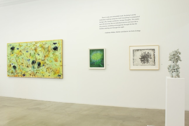 Photograph of a detail view of an exhibition with three paintings hung on a white wall and a sculpture on a pedestal in front