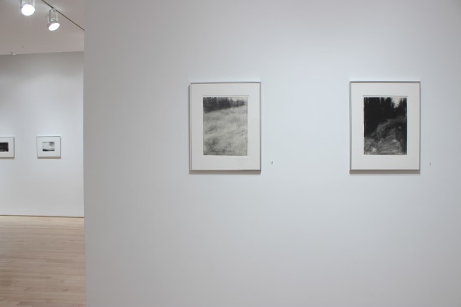 Photograph showing a view of an exhibition space, with two drawings hanging on a white wall