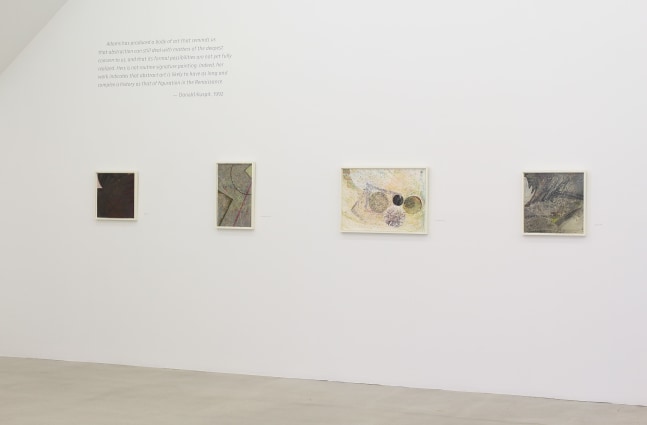Photograph showing a view of an exhibition space, with four paintings hanging on a white wall