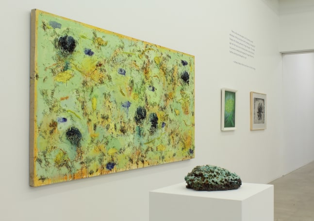 Photograph of a detail view of an exhibition, with one large painting and two smaller paintings hung on a white wall, with an organic-looking sculpture on a pedestal in front