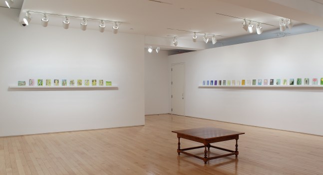 Photograph showing a corner view of an exhibition space, each wall holding dozens of small paintings on a long shelf