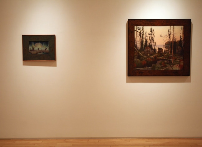 Photograph showing a view of an exhibition space, with two framed paintings hanging on a white wall