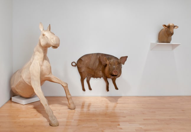 Photograph showing a view of an exhibition space, with a large sculpture emerging from the corner, one hanging on the wall, and a third on a shelf on the wall