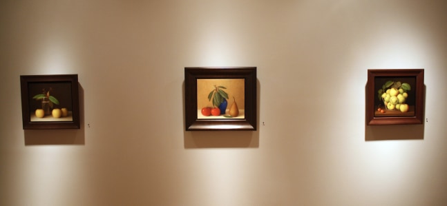 Photograph showing a view of an exhibition, with three small framed paintings hanging on a wall
