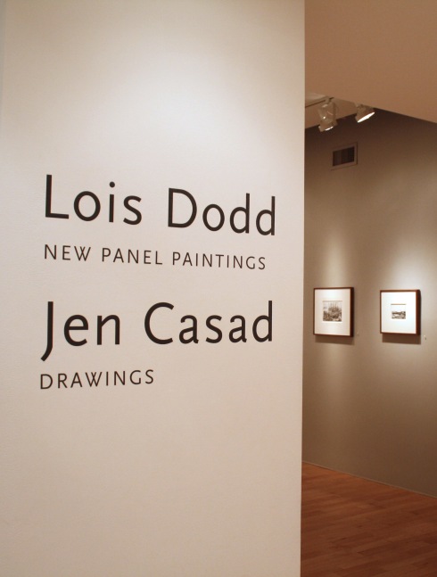 Photograph showing a view of an exhibition space, with two pieces of wall text; one reading &quot;Lois Dodd: New Panel Paintings&quot; and the other reading &quot;Jen Casad: Drawings,&quot; with two small framed drawings in the background