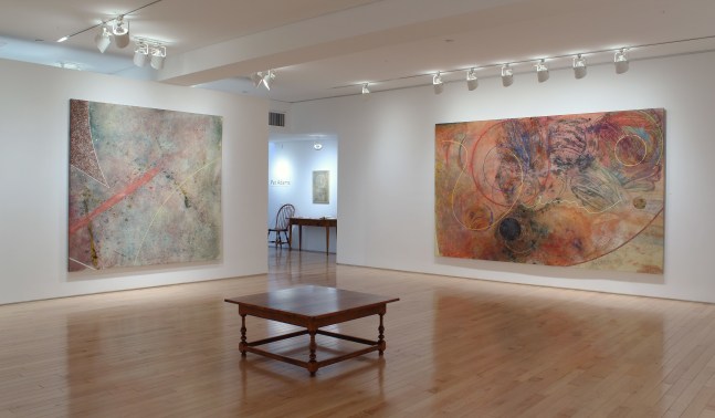 Photograph showing a corner view of an exhibition space, with three paintings hung on white walls