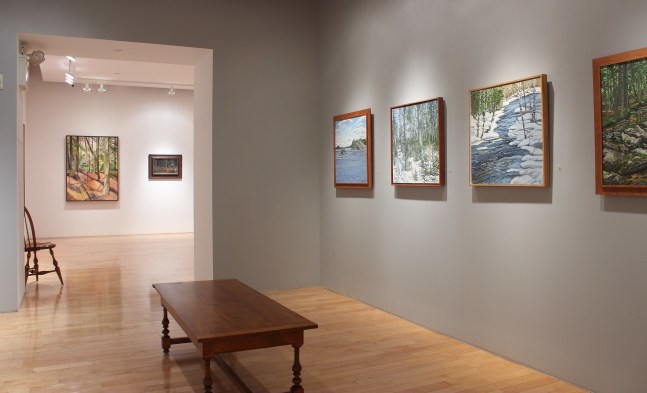 Photograph showing a view of an exhibition space with four framed paintings hanging on a wall