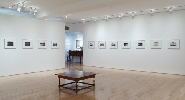 Photograph showing a corner view of an exhibition space, with eleven framed drawings hanging on white walls