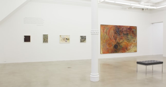 Photograph showing a view of an exhibition space, with five paintings hanging on a white wall