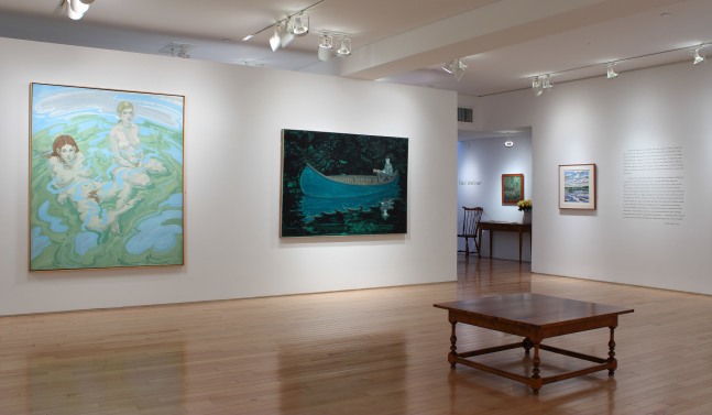 Photograph showing a corner view of an exhibition with three paintings hanging on white walls and a block of exhibition text to the right